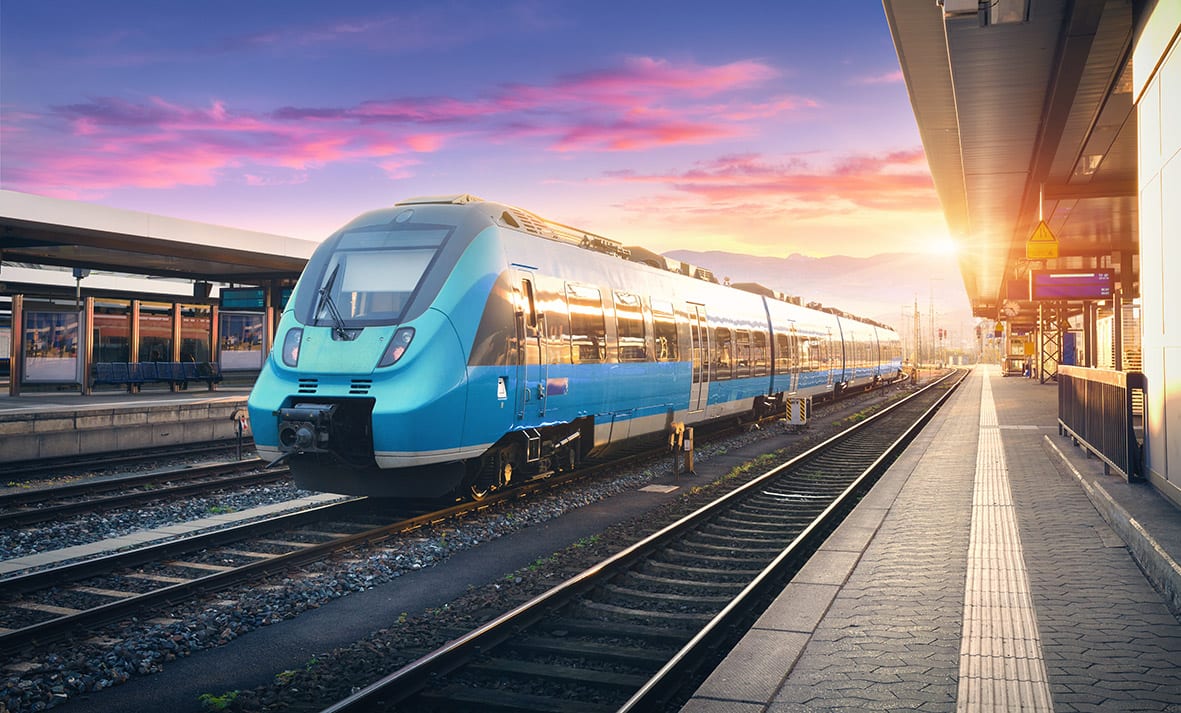 A commuter train standing at a station platform at sunset